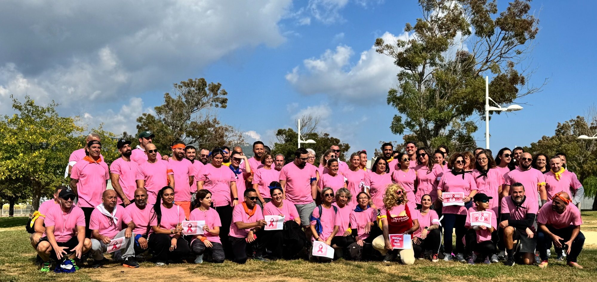 Groupe de personnes portant des t-shirts roses, en tenue de sport, rassemblées dans un parc.